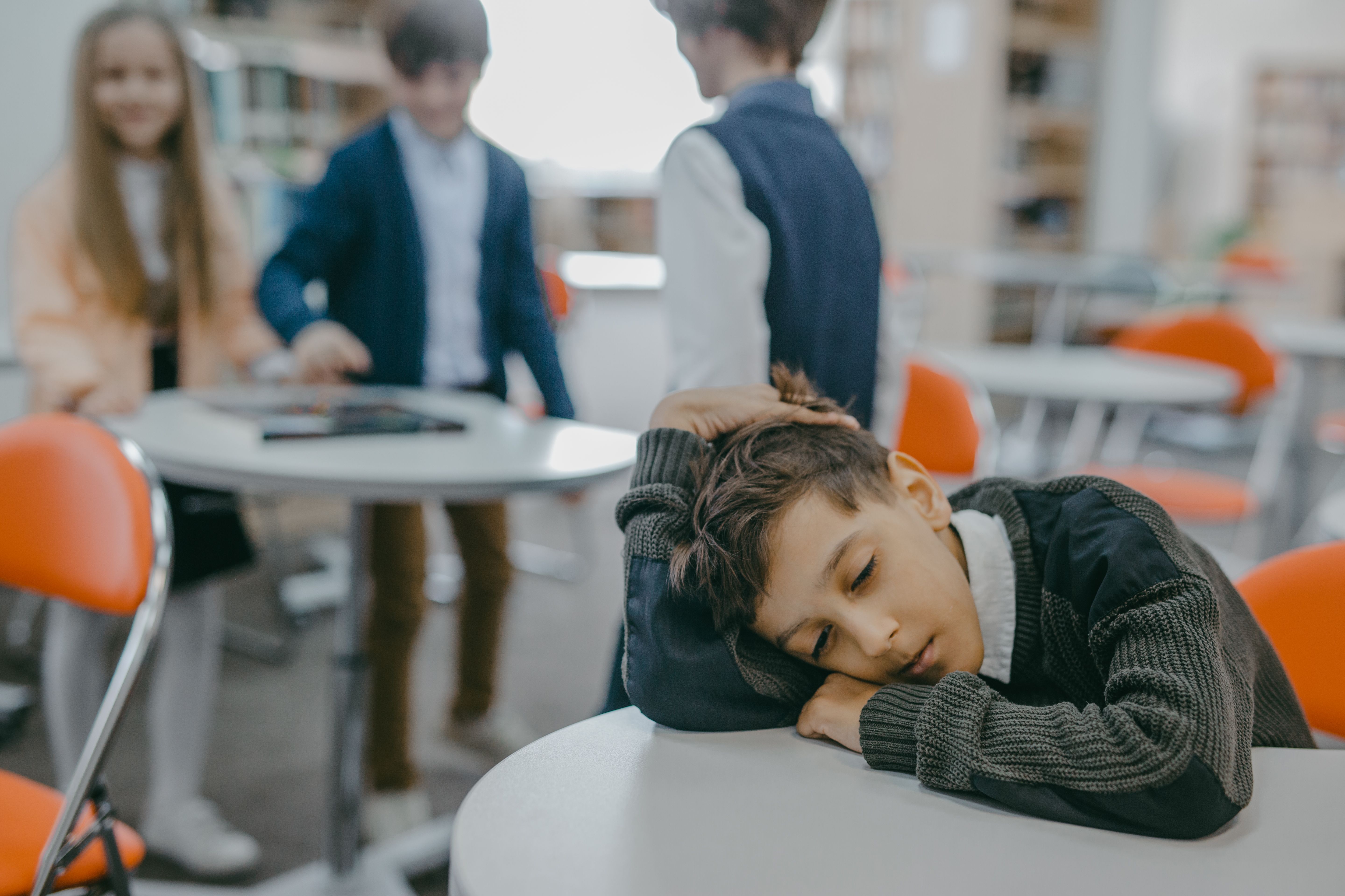 Illustrative stock photograph of a child sitting quietly at a classroom desk, apart from other pupils